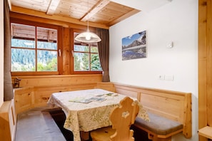 Una cabaña de madera con una mesa de comedor, bancos, un ventanal con vistas a un bosque y un cuadro en la pared.