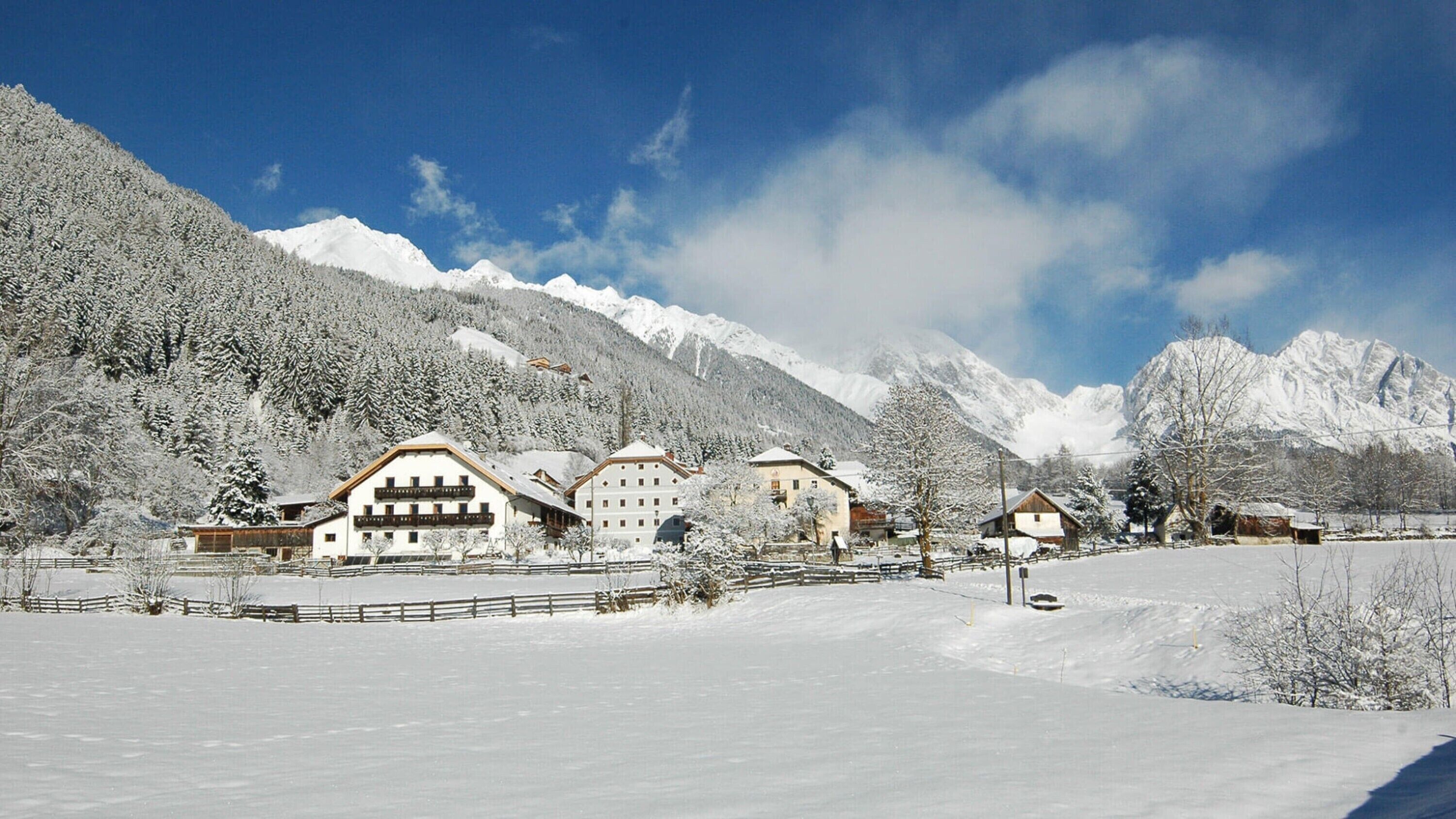 A snow-covered mountain resort with chalet-style buildings, a fenced courtyard, and snow-laden trees.