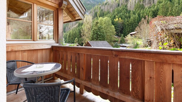Ein hölzerner Balkon mit Tisch und Stühlen mit Blick auf ein bewaldetes Tal.
