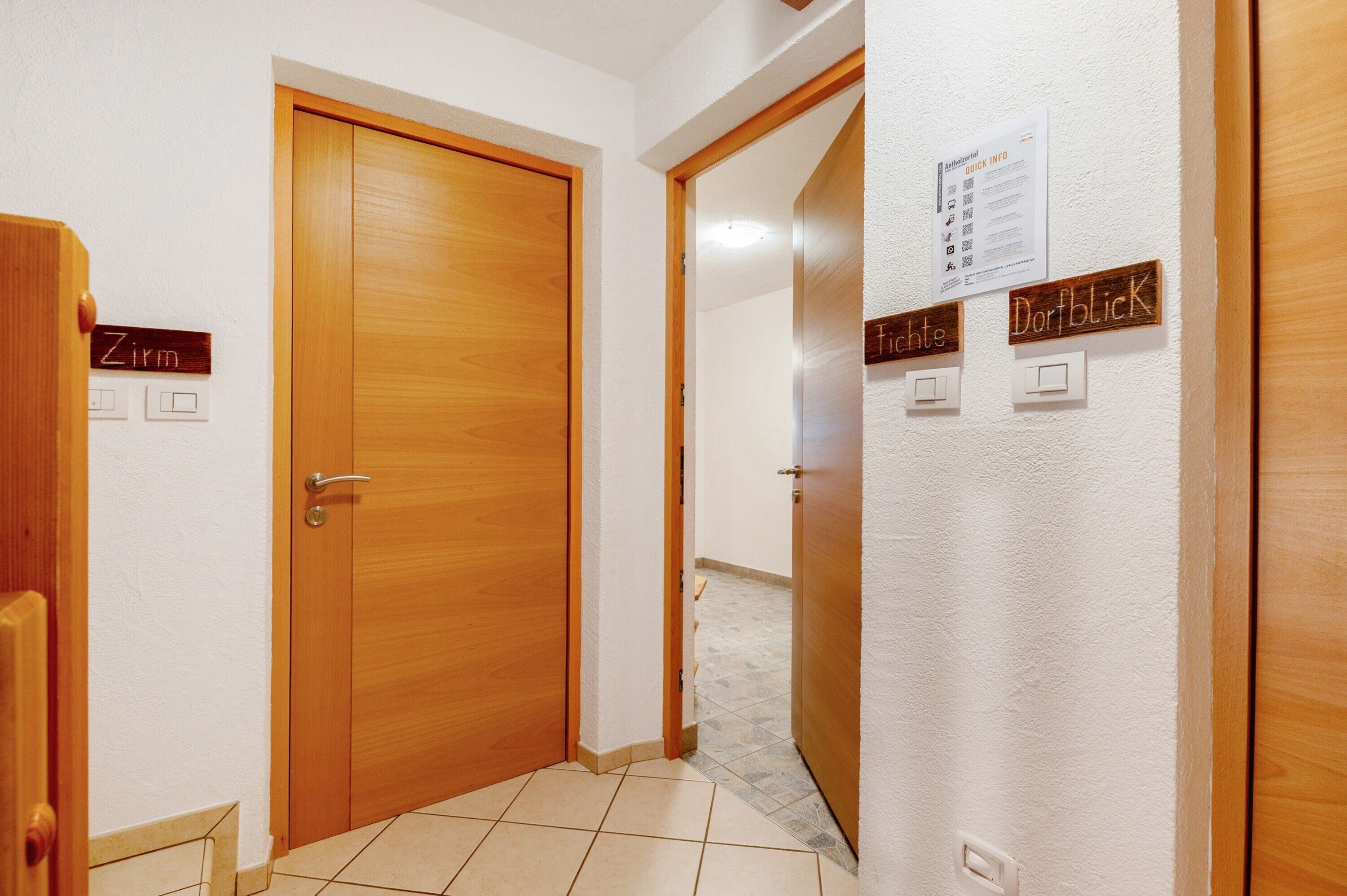 Un couloir avec des portes en bois portant les inscriptions « Zimmer » et « Dorfblick », et un panneau mural indiquant « Informations rapides ».