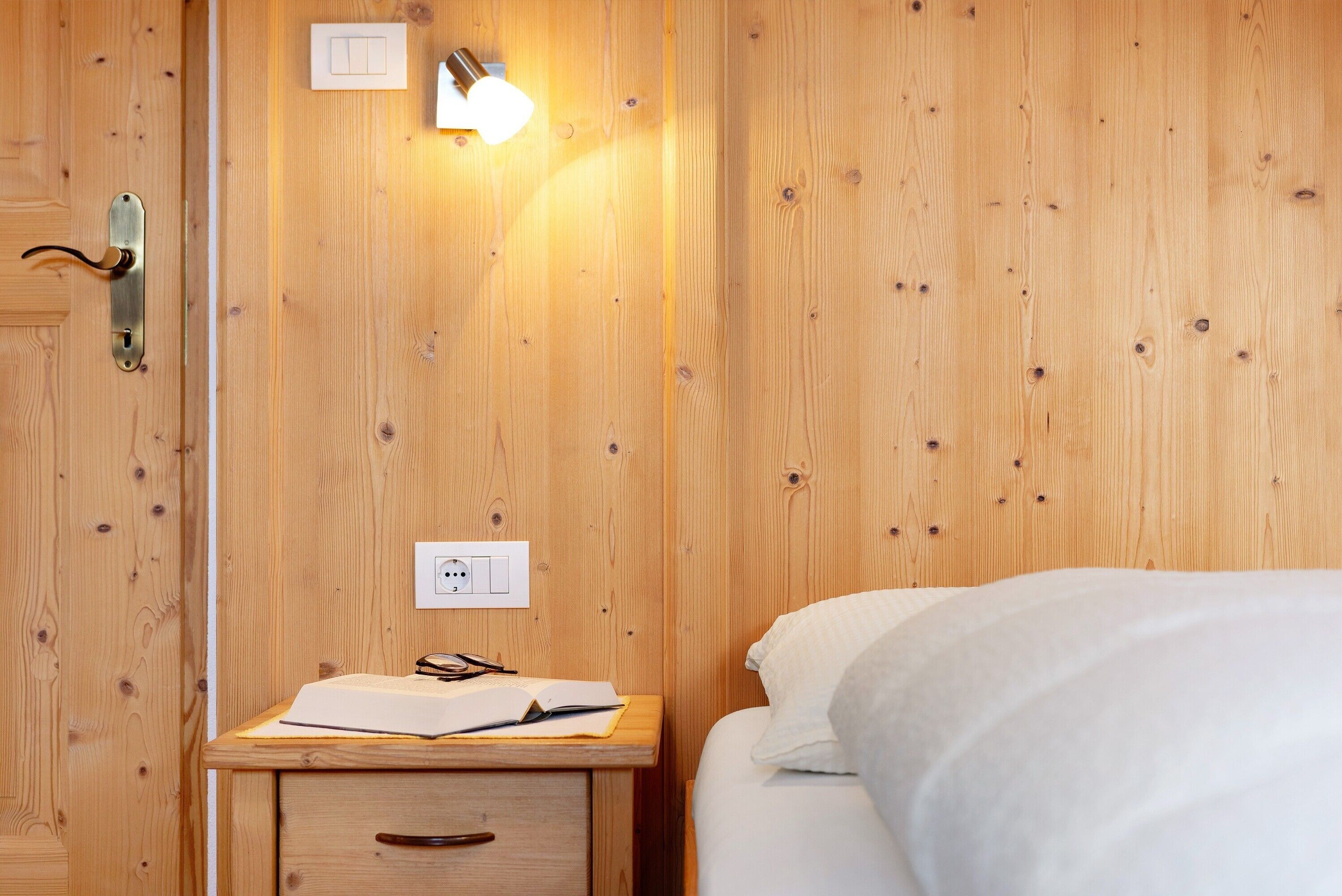 Une pièce aux murs lambrés, avec un lit, une table de chevet dotée d’une lampe et une prise de courant.