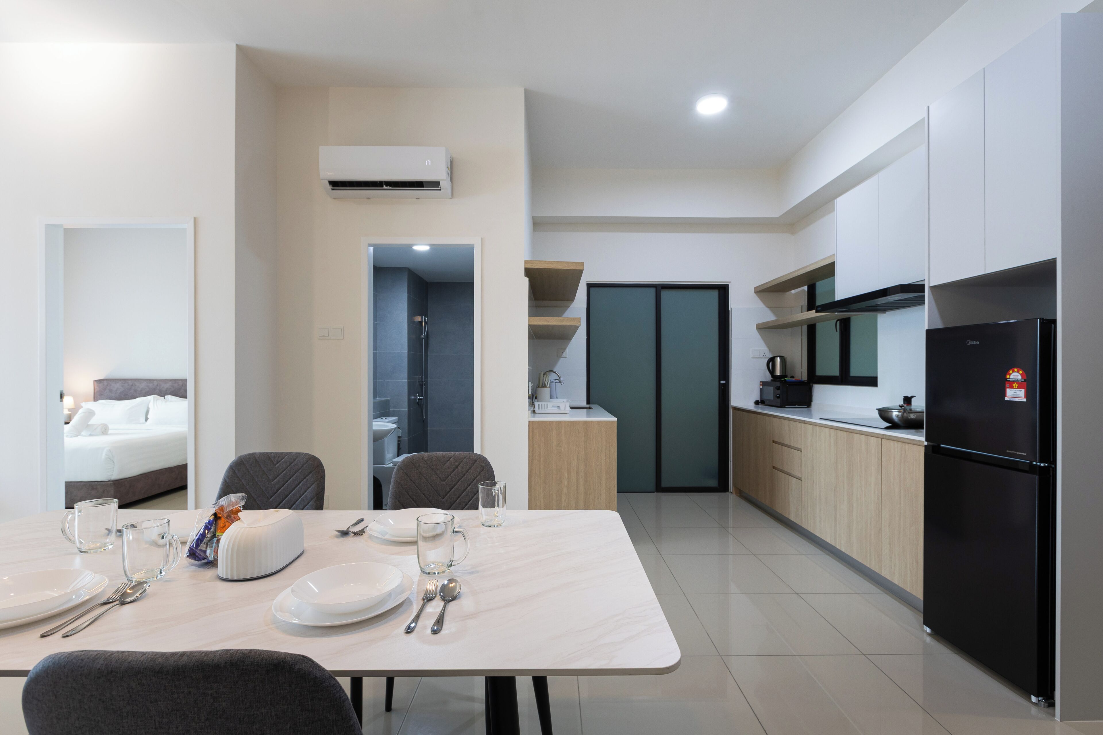 A modern hotel room with a dining area, kitchenette, and a separate bathroom.
