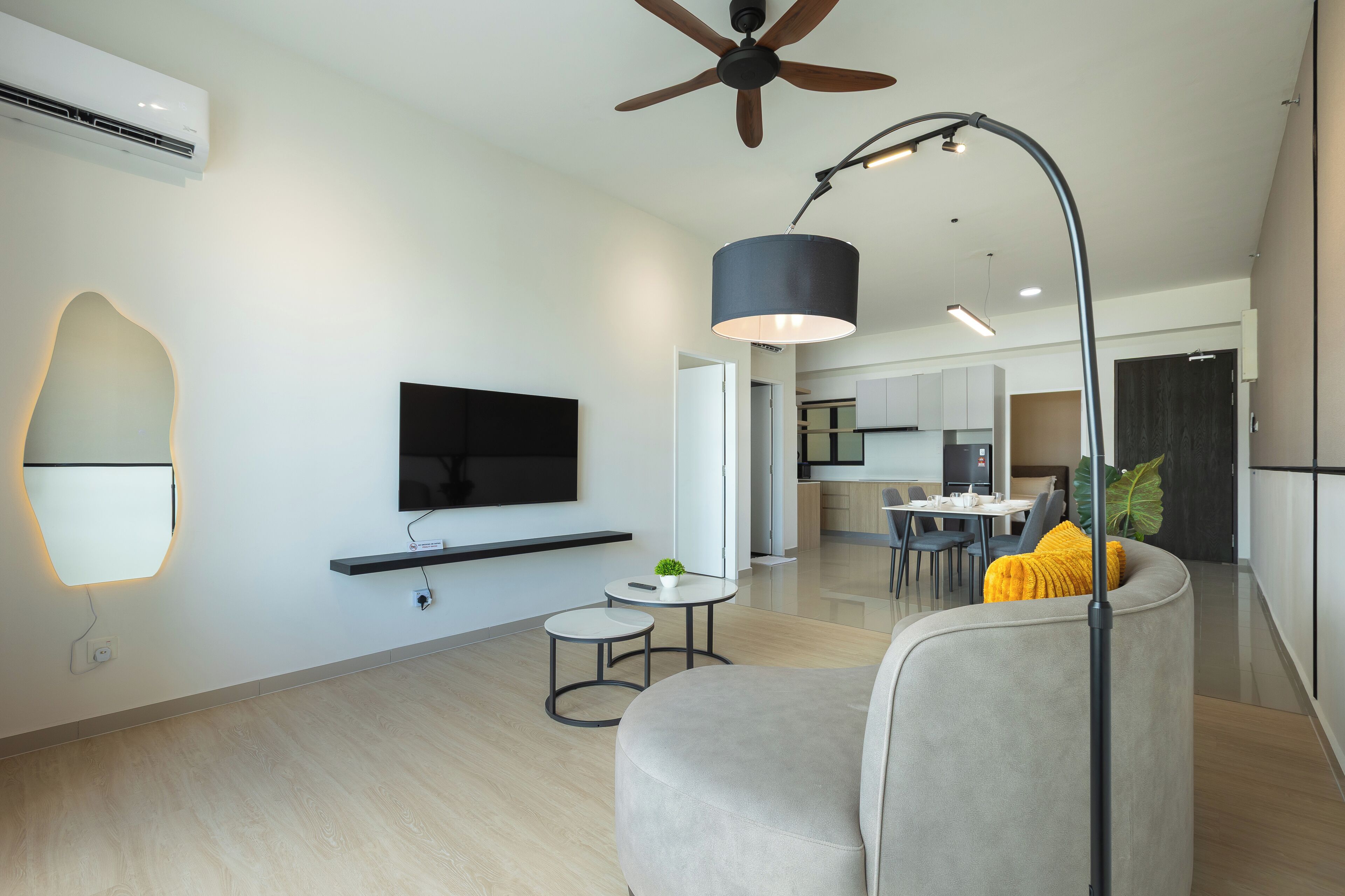 A modern living room with a flat-screen TV, a ceiling fan, and a dining area in the background.