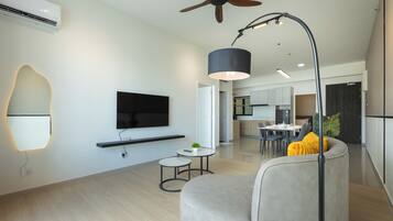 A modern living room with a flat-screen TV, a ceiling fan, and a dining area in the background.