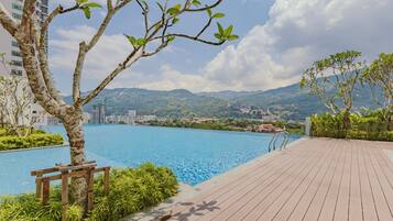A swimming pool with a wooden deck, surrounded by greenery and overlooking a mountainous landscape.