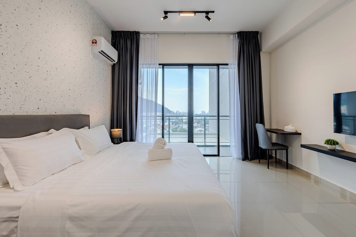 Una habitación de hotel moderna con una cama grande, un escritorio, una silla, un televisor y un balcón con vista a la ciudad.