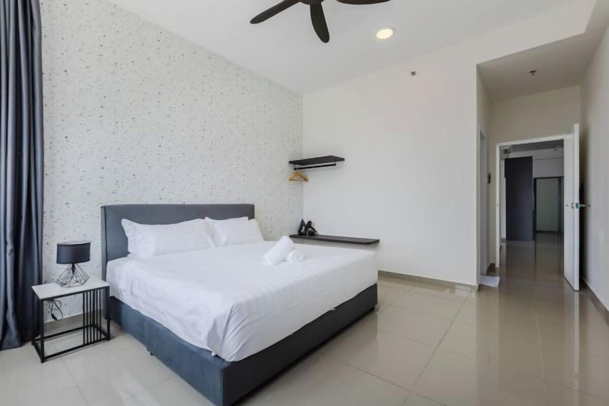 Une chambre d’hôtel moderne avec un grand lit, une table de chevet avec une lampe, un ventilateur de plafond et une vue sur un couloir.