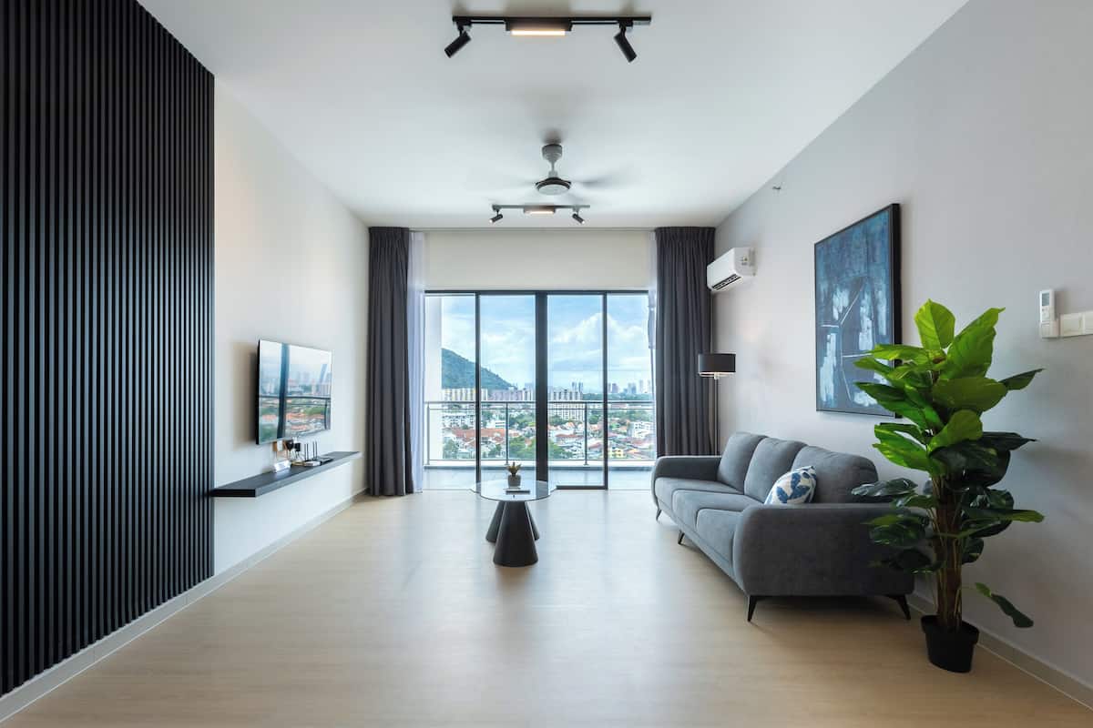 Una sala de estar moderna con un ventanal grande, un sofá gris, una mesa de centro negra y una planta en maceta.