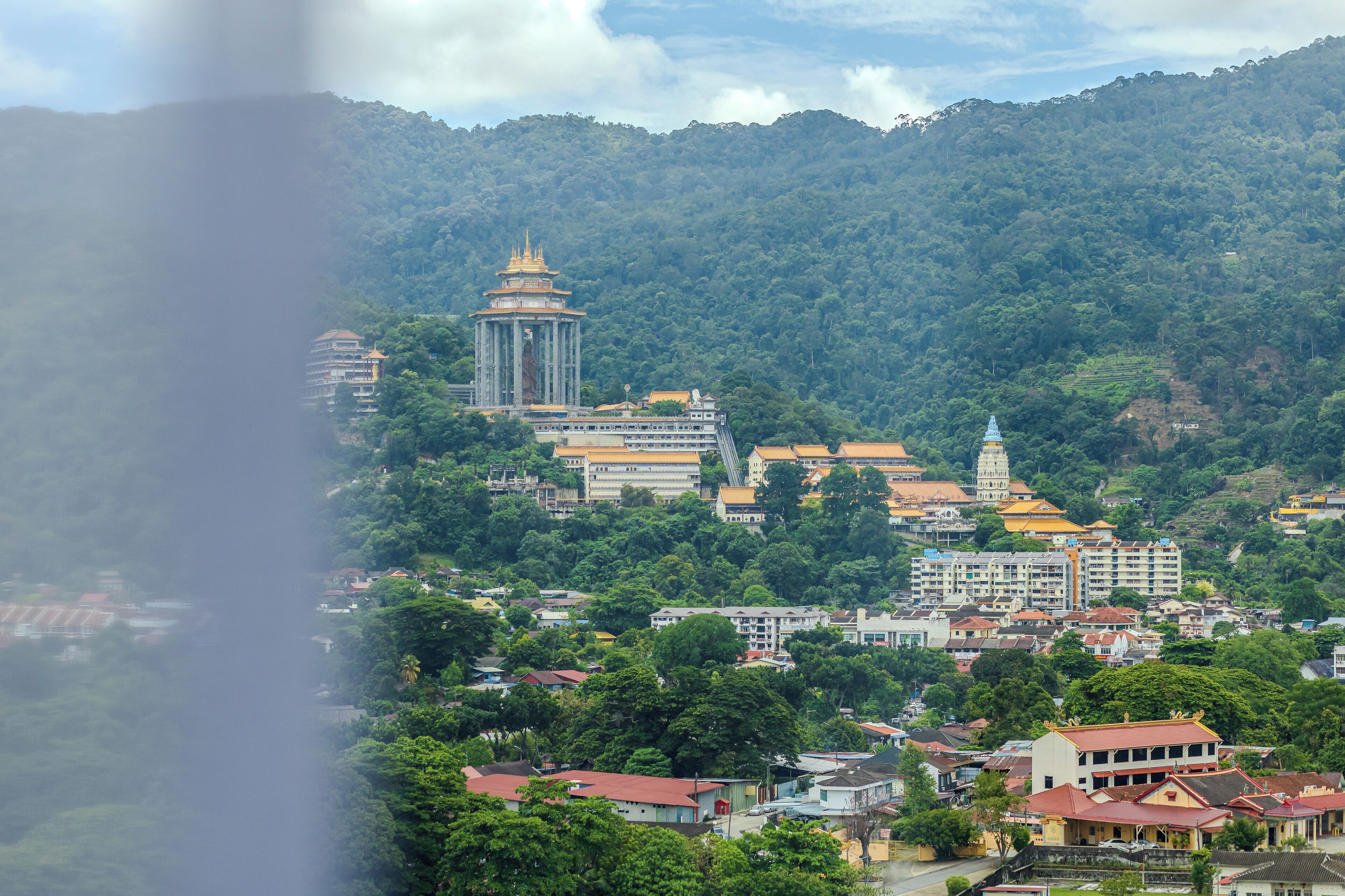 A cityscape with a prominent pagoda-like structure, dense greenery, and a mix of traditional and modern buildings.