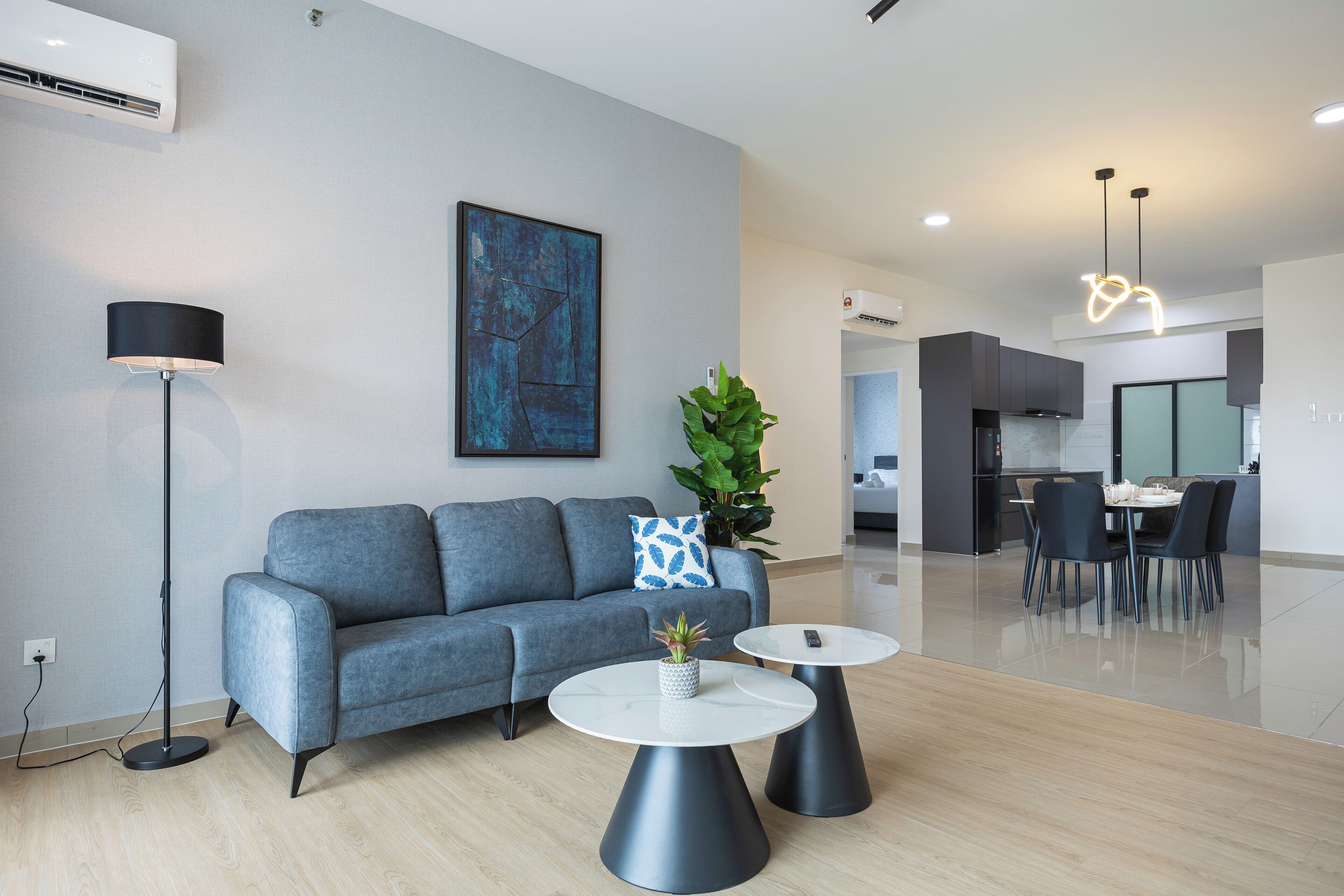 A modern living room with a grey sofa, two round tables, a floor lamp, and a painting on the wall.
