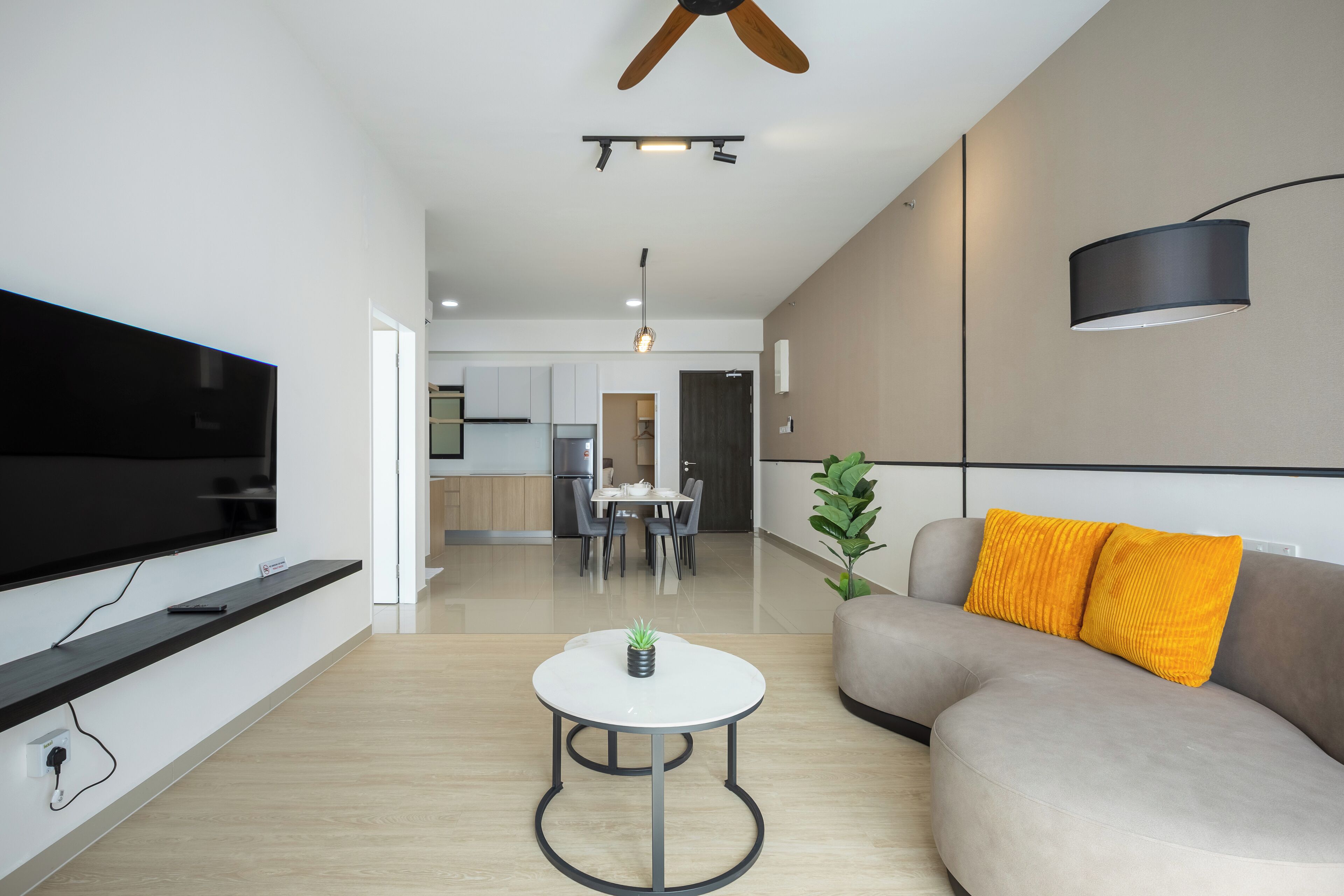A modern living room with a flat-screen TV, a round coffee table, a sofa with yellow cushions, and a ceiling fan.