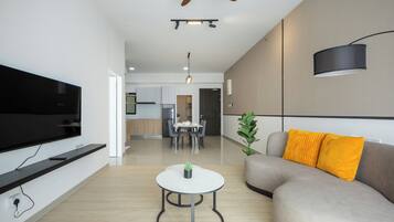 A modern living room with a flat-screen TV, a round coffee table, a sofa with yellow cushions, and a ceiling fan.