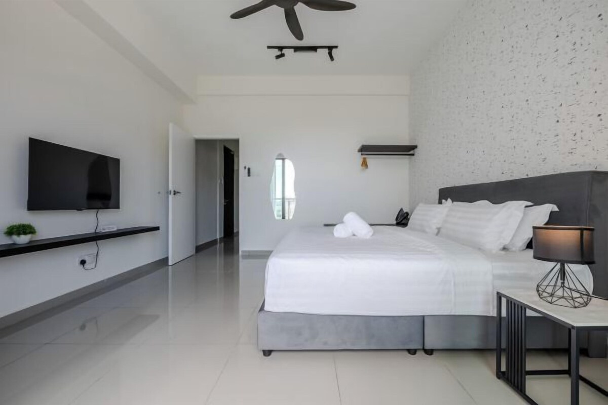 A modern bedroom with a large bed, a flat-screen TV mounted on the wall, and a ceiling fan.