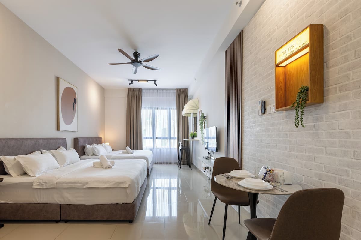Habitación de hotel con cama, dos mesitas de noche, escritorio con silla, ventilador de techo y pared de ladrillo con un cartel.