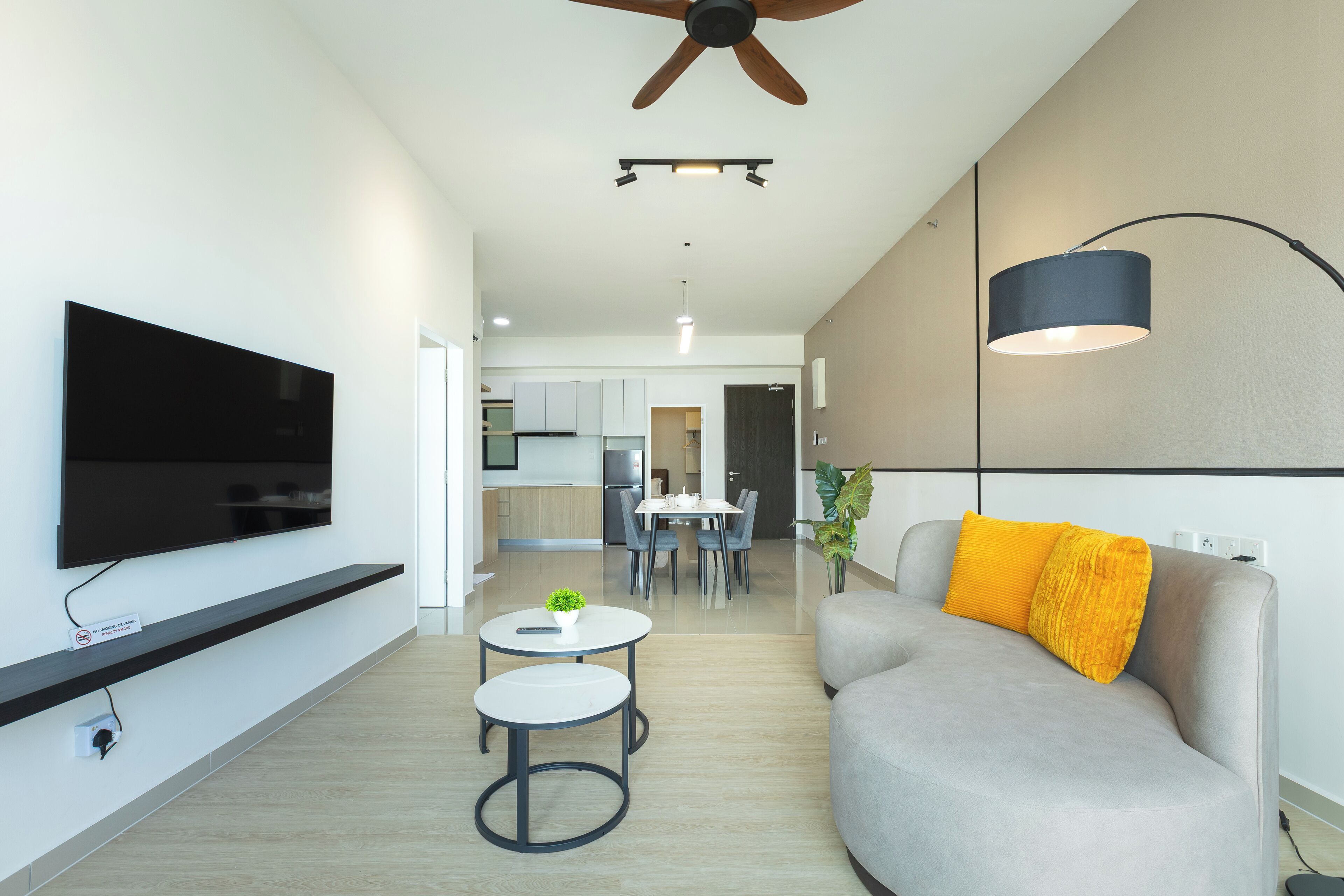 A modern living room with a flat-screen TV, a ceiling fan, a dining area, and a sofa with a cushion.