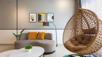 A modern living room with a grey sofa, a round coffee table, a hanging rattan chair, and three abstract wall art pieces.
