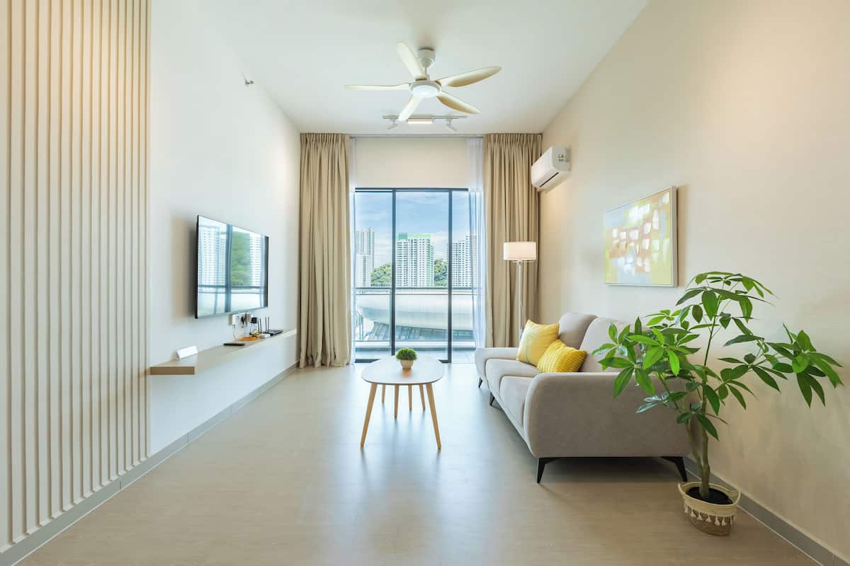 Una sala de estar moderna con un sofá, una mesa de centro, una planta en maceta, un ventilador de techo y un amplio ventanal con vistas a la ciudad.