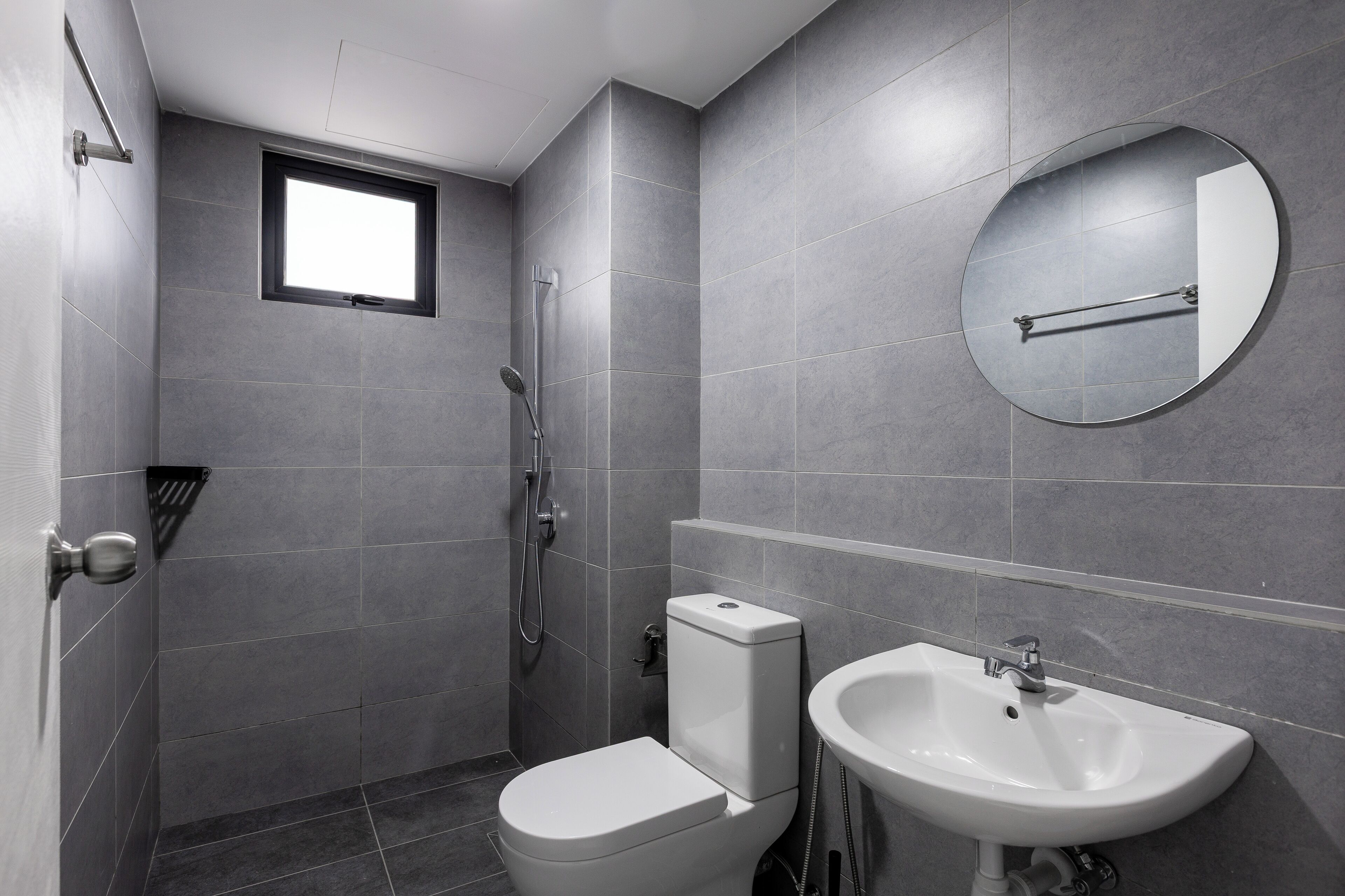 Um banheiro moderno com azulejos cinzas, vaso sanitário, pia e chuveiro.