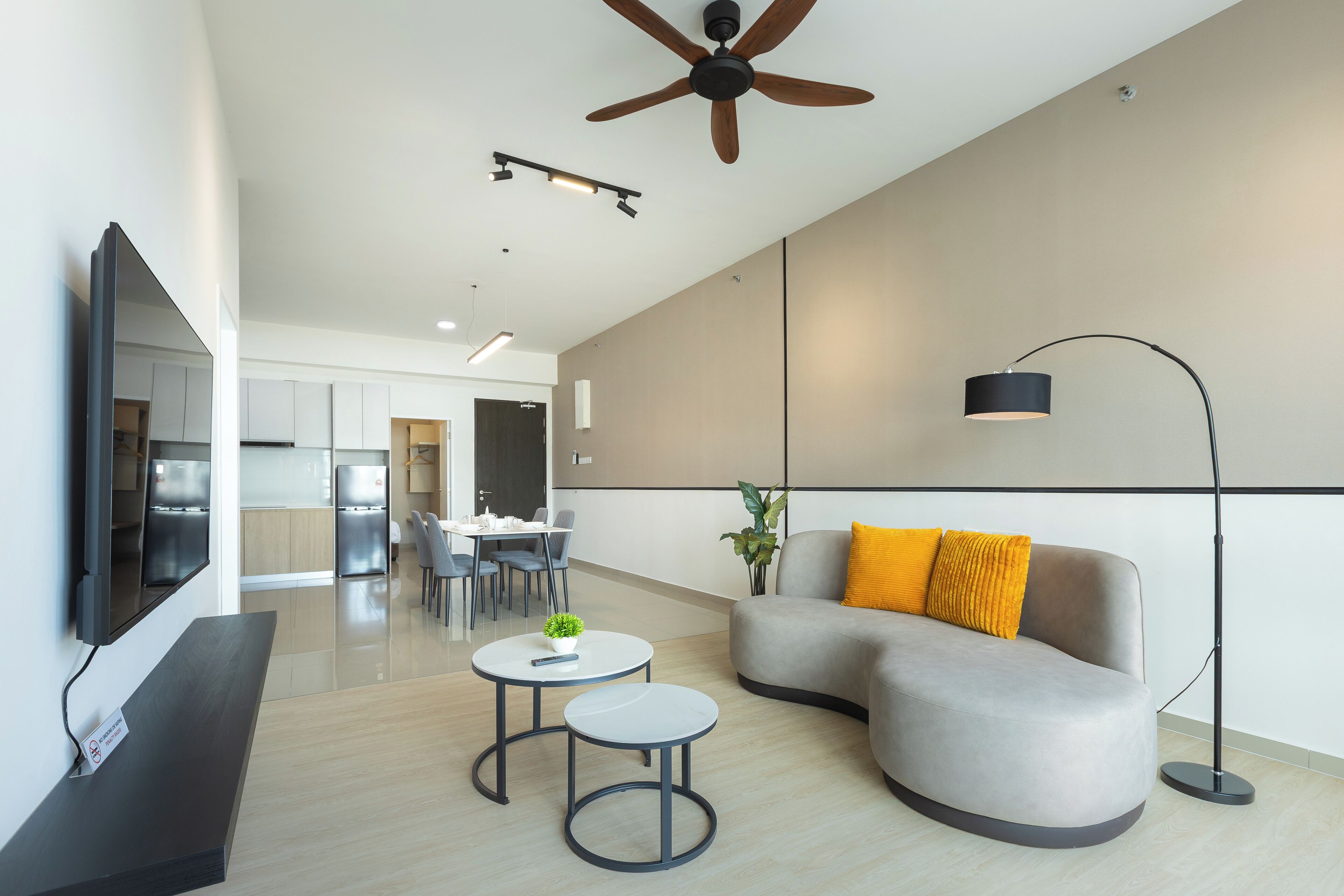A modern living room with a curved grey sofa, two round tables, a flat-screen TV, and a ceiling fan.