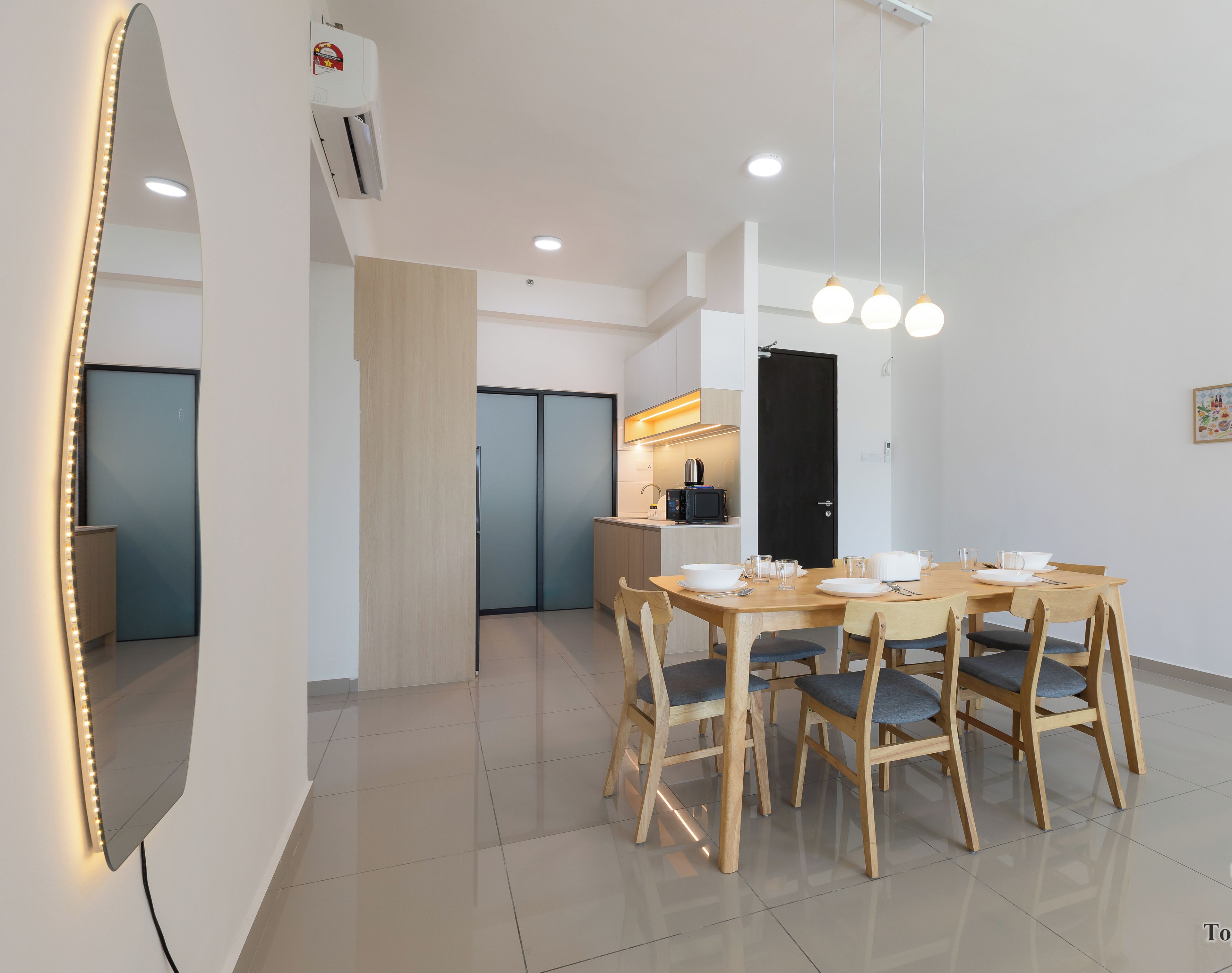 A modern dining area with a wooden table and chairs, a kitchen in the background, and a black door.