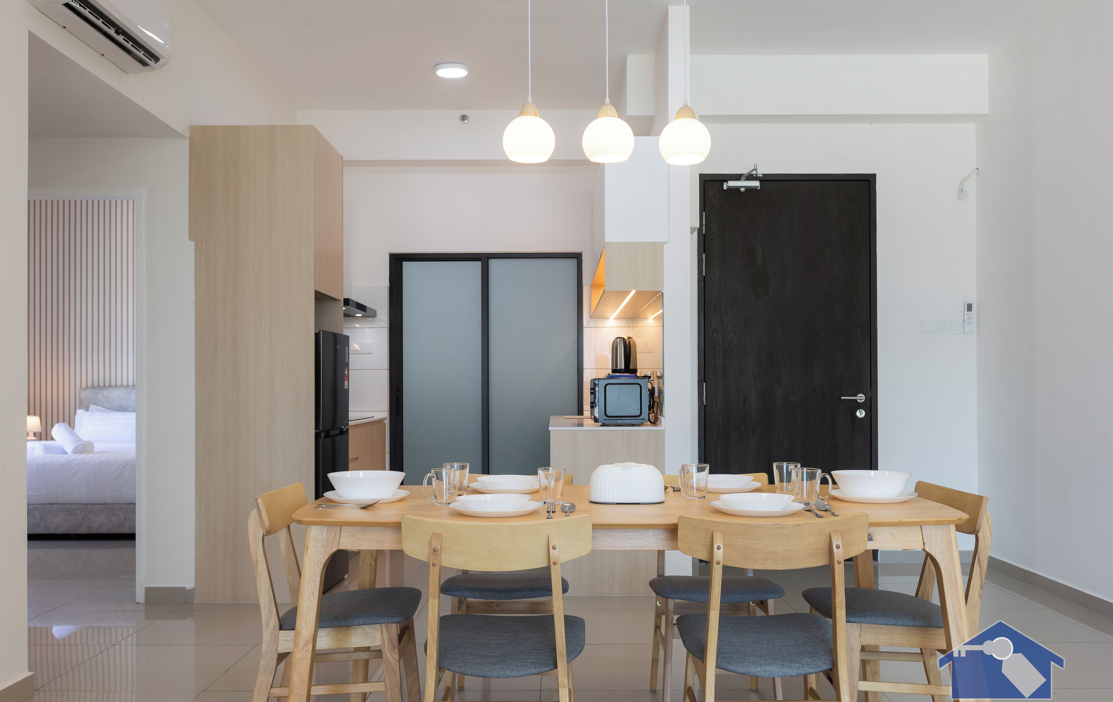 A modern dining area with a wooden table set for four, a television, and a kitchen in the background.
