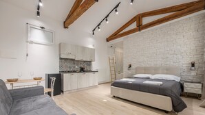 A modern bedroom with a bed, a sofa, a kitchen area, and a white brick wall. - Mangano Suite Apartment (Palermo)