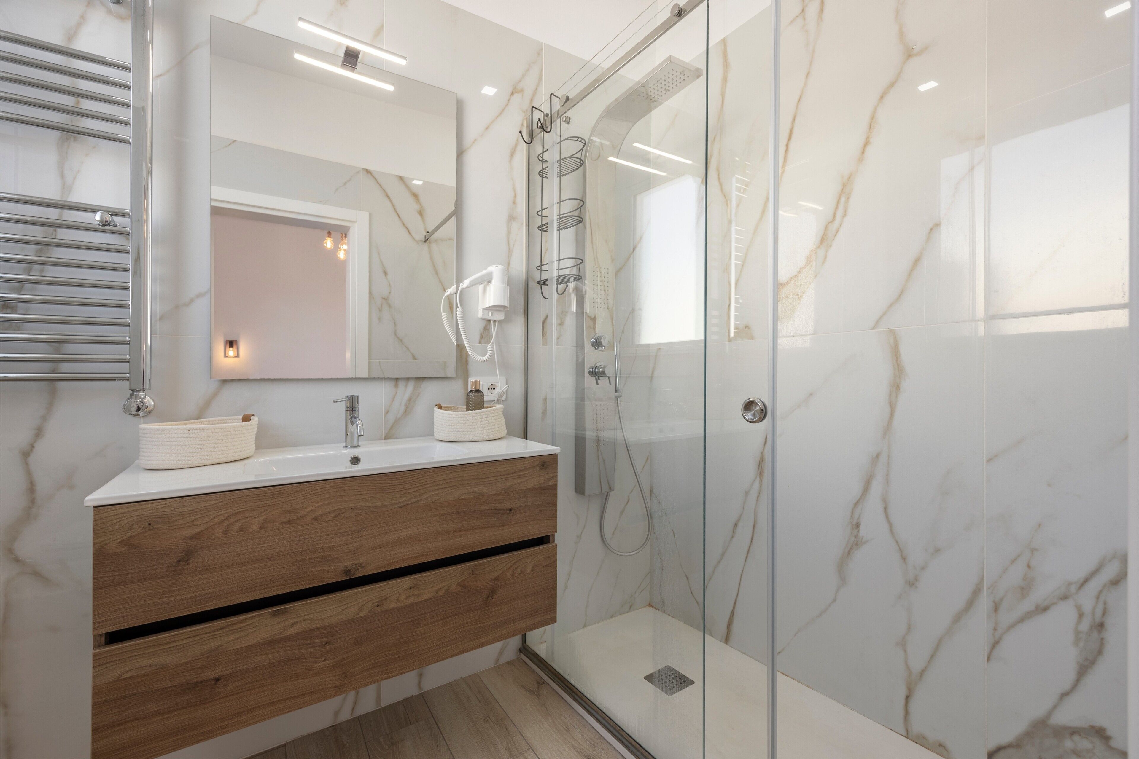 Une salle de bain moderne avec une douche à parois de verre, des murs en marbre, un meuble-lavabo en bois et un grand miroir.