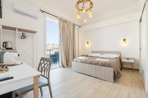 Una habitación de hotel moderna con una cama, un escritorio, una silla, un balcón con vistas y una araña.