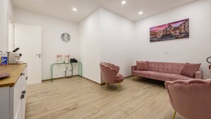 A modern room with a wooden floor, a pink sofa, a pink armchair, a glass side table, a painting on the wall, and a clock. - Mangano Suite Apartment (Palermo)