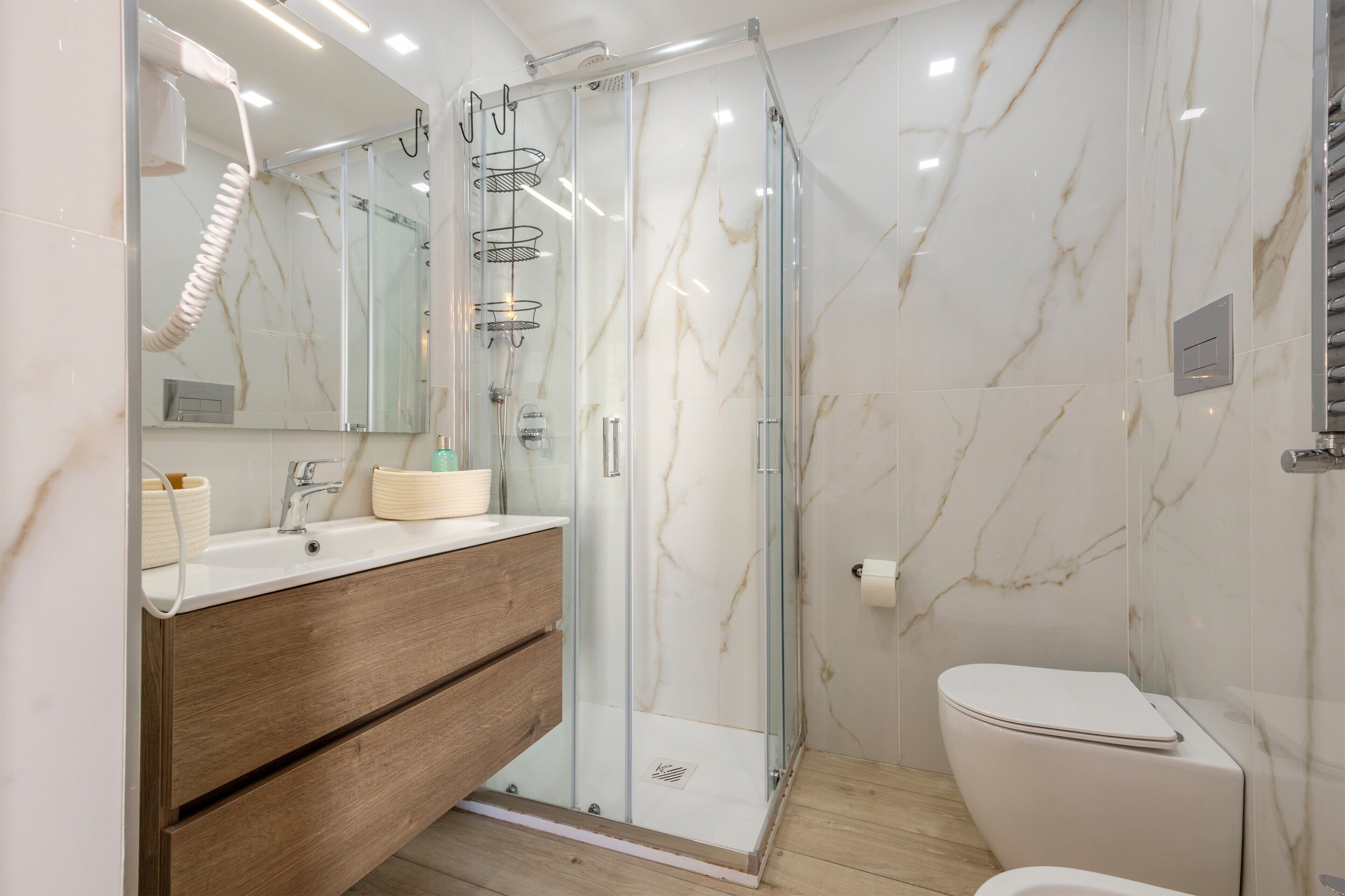 A modern bathroom with a glass-enclosed shower, a wooden vanity, and a white toilet.