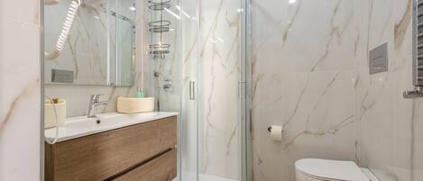 A modern bathroom with a glass-enclosed shower, a wooden vanity, and a white toilet.
