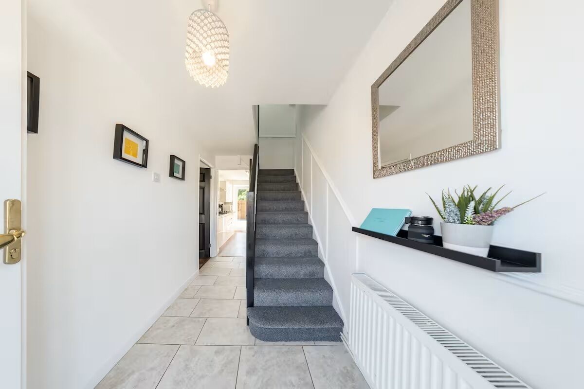 A modern hallway with a staircase, a mirror, and a shelf with decorative items.