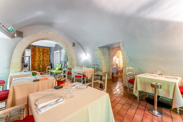 A restaurant with multiple tables, some with red cushions, and a stone archway.