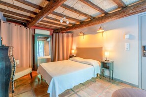 Un dormitorio con una cama, dos mesitas de noche con lámparas, una silla, techo de madera y una puerta.