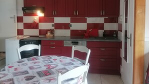 A compact kitchen with red cabinets, a white tiled backsplash, and a table with a patterned tablecloth. - Large T2 in villa with sea view and spa not overlooked (La Ciotat)