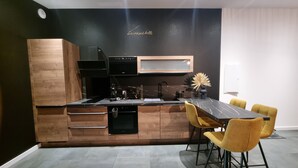 Een moderne keuken met houten kasten, een ingebouwde oven en een eethoek met een marmeren tafel en gele stoelen.