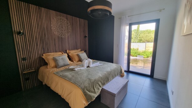 Een moderne slaapkamer met een bed, een nachtkastje, een hanglamp en uitzicht op het buitengebied door een schuifdeur.