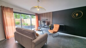 Een moderne woonkamer met een bank, een fauteuil, een televisie en een eettafel.