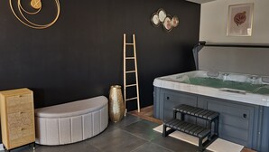 Een moderne badkamer met een zwarte wand, een houten kast, een ronde bank, een gouden vaas, een ladder, een badkuip en wanddecoratie.