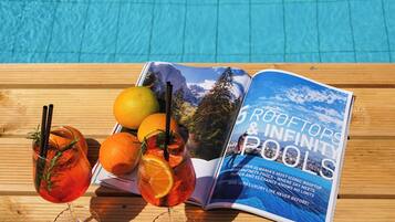 A magazine titled "ROOFTOPS & INFINITY POOLS" on a wooden table by a pool.