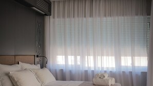 Un dormitorio con una cama grande, cabecera, aire acondicionado de pared y cortinas traslúcidas.