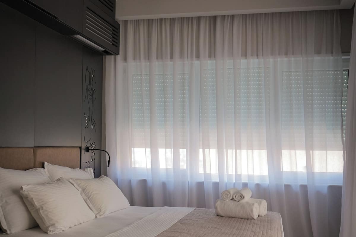 Une chambre à coucher avec un grand lit, une tête de lit, un climatiseur fixé au mur et des rideaux légers.