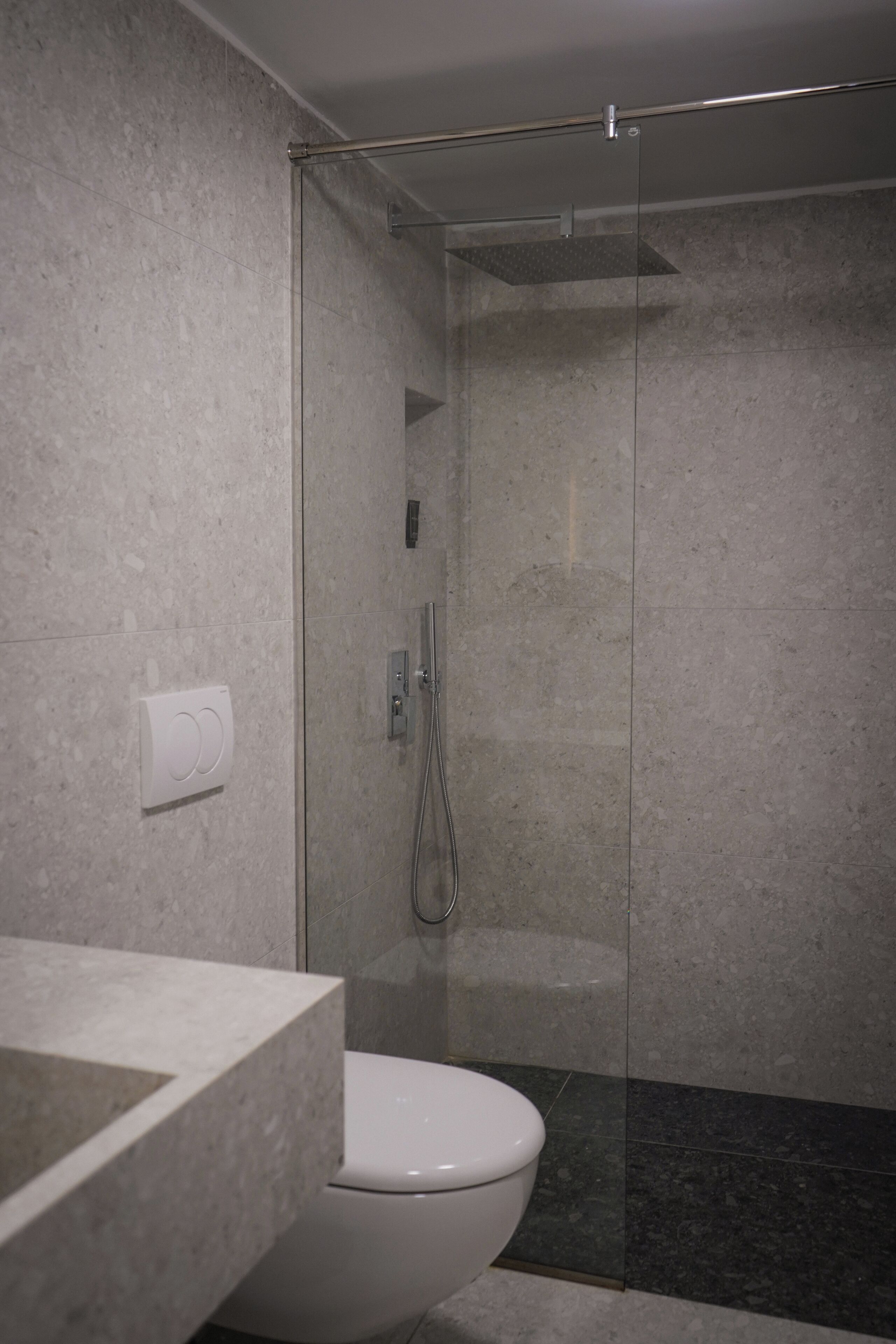 A modern bathroom with a glass-enclosed shower, a white toilet, and a marble countertop.