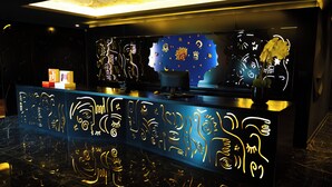 Un mostrador de recepción con arte mural iluminado y un jarrón de flores.