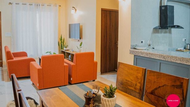 A modern living room with orange sofas, a wooden dining table, and a kitchen area with a stove and sink.