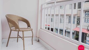 A wicker chair by a window with a view of buildings and a red umbrella.