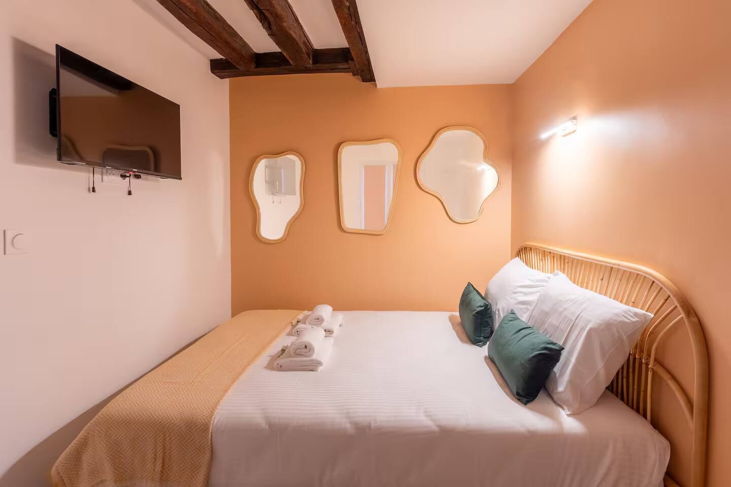 Une chambre d’hôtel avec un lit, un téléviseur fixé au mur et trois miroirs également fixés au mur.