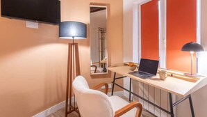 Una habitación con escritorio, computadora portátil, silla, lámpara de pie y televisor montado en la pared.