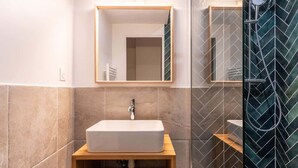 Un baño con un lavamanos rectangular, un espejo encima y una zona de ducha con diseño de espiga.