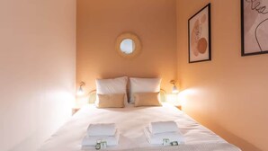 Una cama bien hecha con sábanas blancas, un espejo redondo encima y dos cuadros en las paredes.